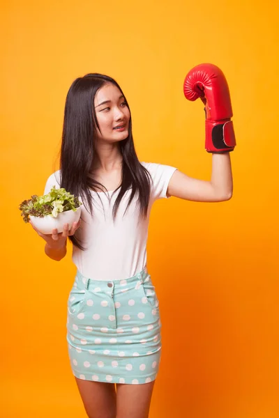 年轻的亚洲妇女与拳击手套和沙拉在明亮的黄色背景 — 图库照片