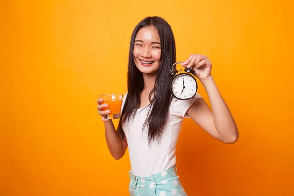 Asian woman with a clock drink orange juice on bright yellow background