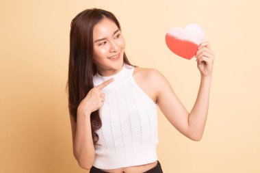 Asyalı kadın bej arka planda kırmızı kalbe işaret ediyor