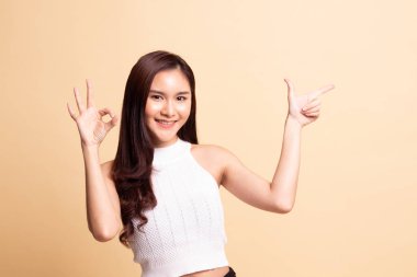 Genç Asyalı kadın işaret ediyor ve bej arka planda iyi olduğunu gösteriyor