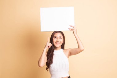 Genç Asyalı kadın bej arka planda boş bir işaret gösteriyor.