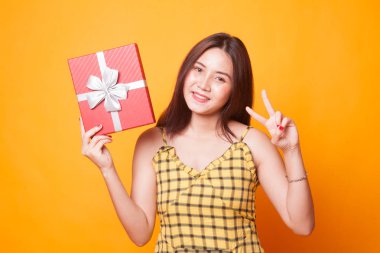 Asyalı kadın sarı arka plan üzerinde zafer işareti bir hediye kutusu ile göster