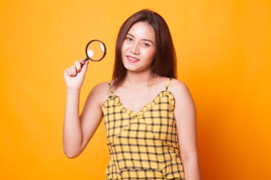 Sarı arka plan üzerinde büyüteçle genç Asyalı kadın