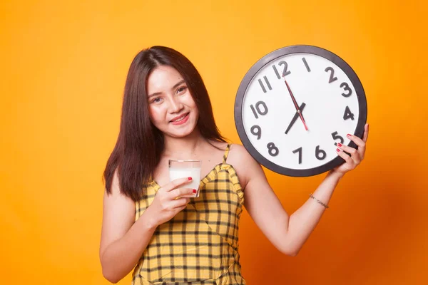 ミルクのアジアの女性の健康的な飲料のガラスは黄色の背景に時計を保持します — ストック写真