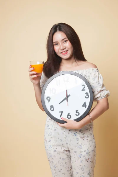 Asian woman with a clock drink orange juice on beige background