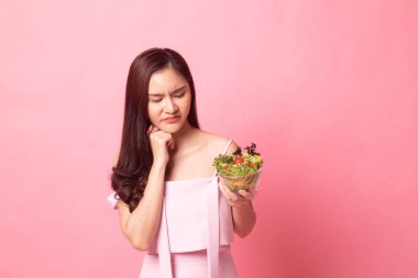 Genç Asyalı kadın mutlu değil nefret ediyorum pembe bir arka plan üzerinde salata