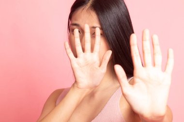 Genç Asyalı kadın yüzünü pembe arka planda saklıyor.