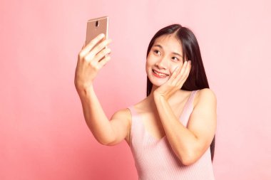 Pembe arka planda cep telefonu olan genç Asyalı kadın selfie 'si.