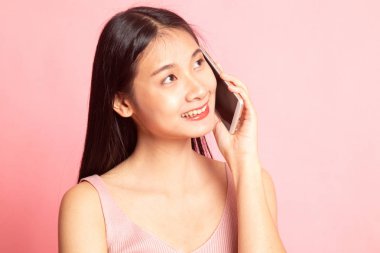 Pembe arka planda cep telefonuyla konuşan genç Asyalı kadın.