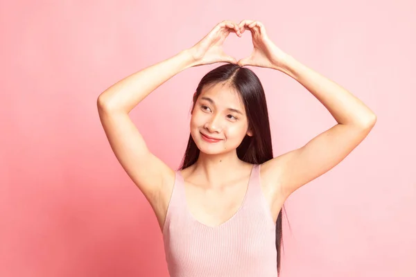 年轻的亚洲女人在粉红的背景上做心脏手势 — 图库照片