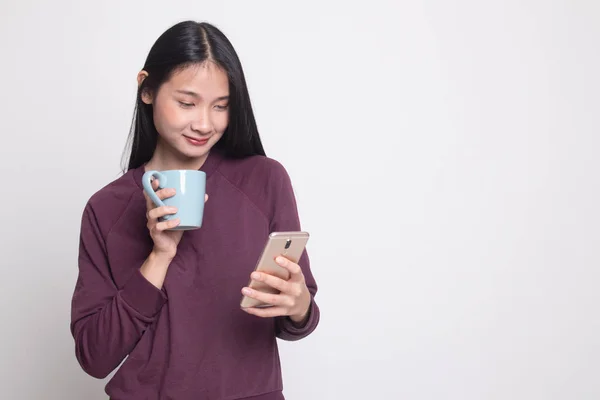 Young Asian woman with mobile phone and coffee cup on white background