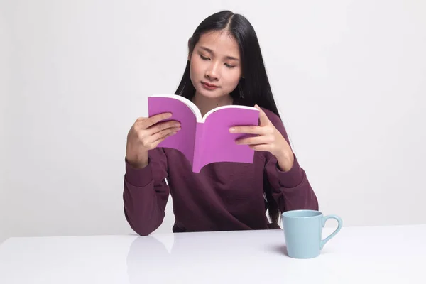 Junge asiatische Frau liest ein Buch mit einer Tasse Kaffee. — Stockfoto