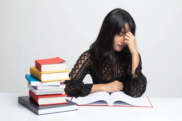 Mujer asiática agotada tiene dolor de cabeza leer un libro con libros en la pestaña —  Fotos de Stock