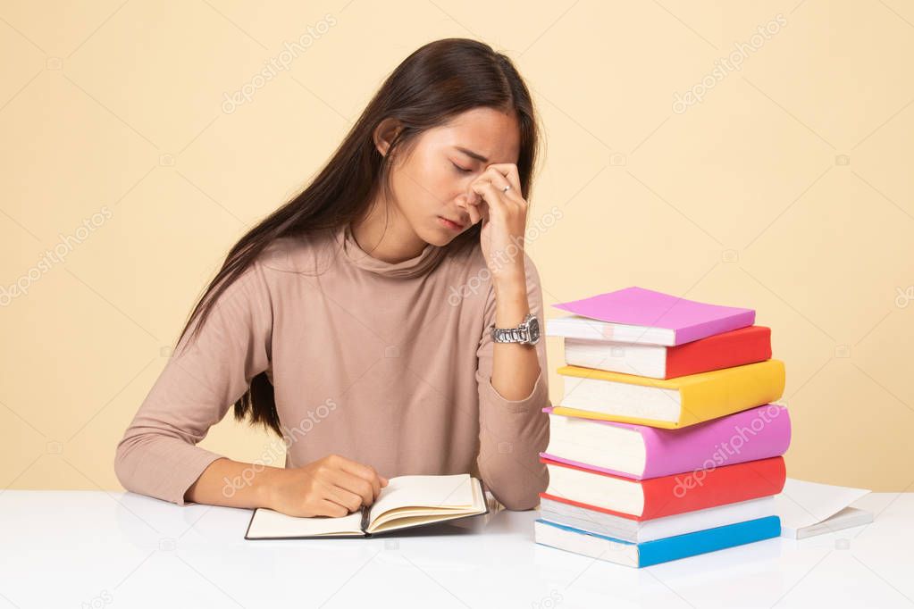Exhausted Asian woman got headache read a book with books on tab