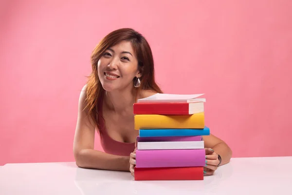 Glückliche junge Asiatin liest ein Buch mit Büchern auf dem Tisch. — Stockfoto