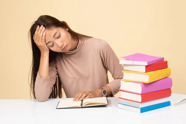 Utmattad ung asiatisk kvinna läsa en bok med böcker på bord. — Stockfoto