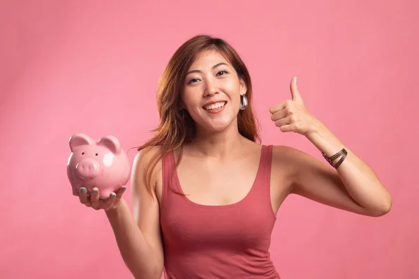 Asian woman thumbs up with pig coin bank.