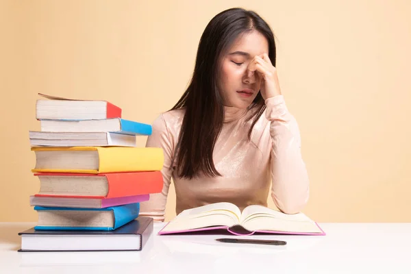 Mujer asiática agotada tiene dolor de cabeza leer un libro con libros en la pestaña — Foto de Stock