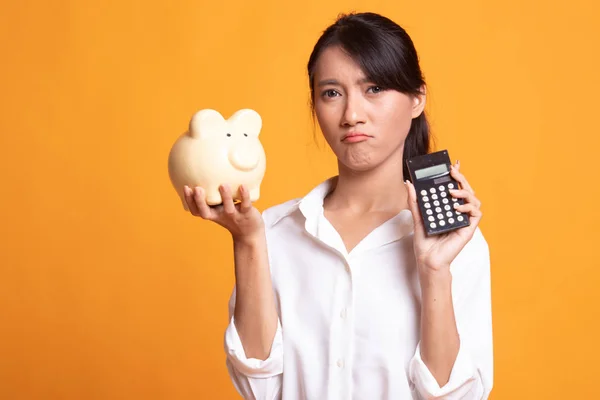 Unglückliche asiatische Frau mit Taschenrechner und Sparschwein. — Stockfoto
