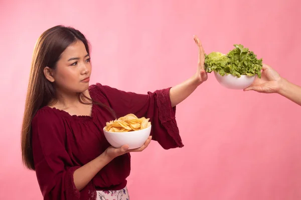 Jonge Aziatische vrouw met aardappel chips nee zeggen tegen salade. — Stockfoto