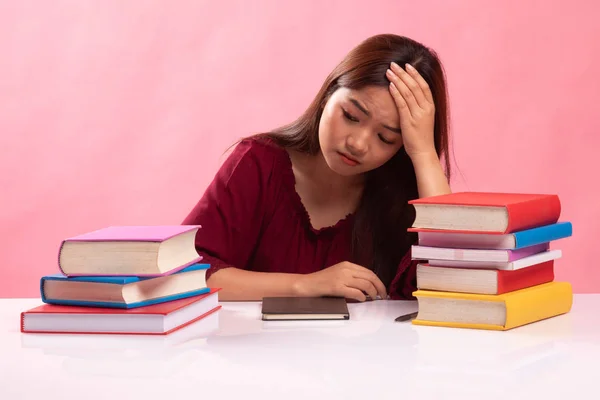 Erschöpfte junge Asiatin liest Buch mit Büchern auf dem Tisch. — Stockfoto