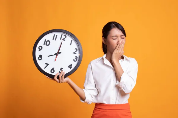 Schläfrige junge asiatische Frau mit einer Uhr am Morgen. — Stockfoto