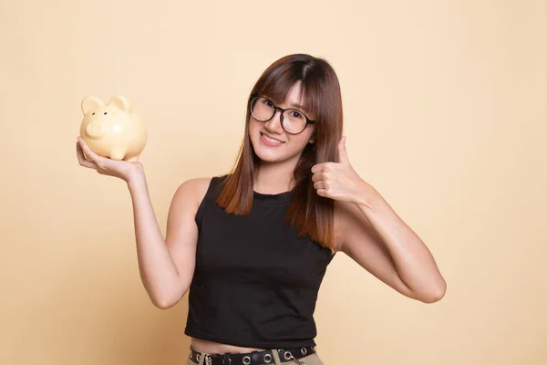 Asian woman thumbs up with pig coin bank.