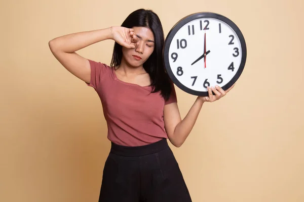 Sleepy young Asian woman with a clock in the morning.