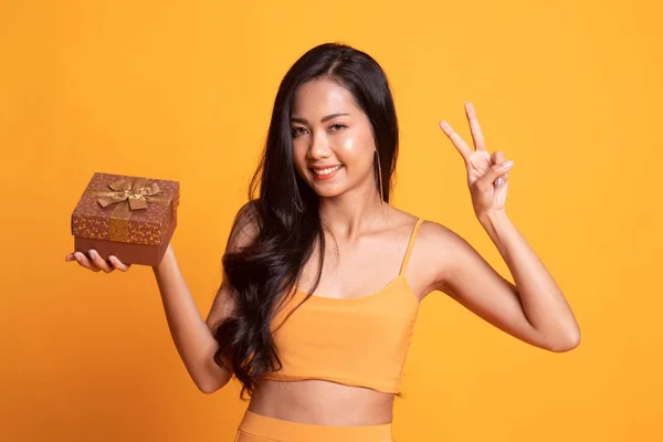 Giovane donna asiatica mostra segno di vittoria con una scatola regalo . — Foto Stock