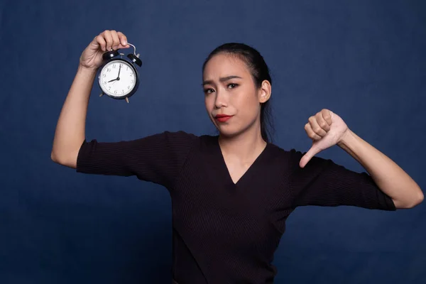 Young Asian woman thumbs down with a clock.
