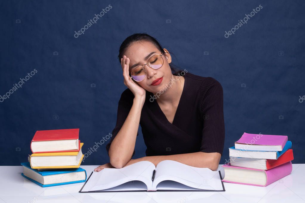 Exhausted Young Asian woman read a book with books on table.