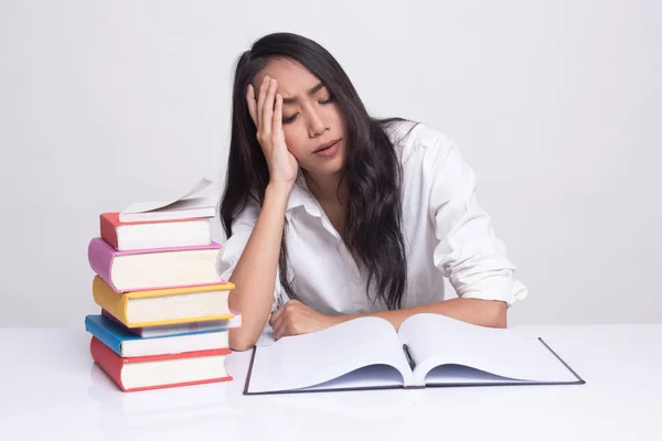 Utmattad ung asiatisk kvinna läsa en bok med böcker på bord. — Stockfoto