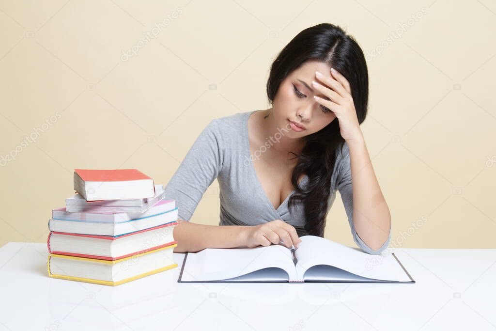 Exhausted Young Asian woman read a book with books on table   on beige background