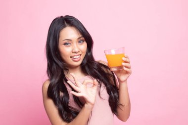 Genç Asyalı kadın pembe arka planda portakal suyu içtiğini gösteriyor.