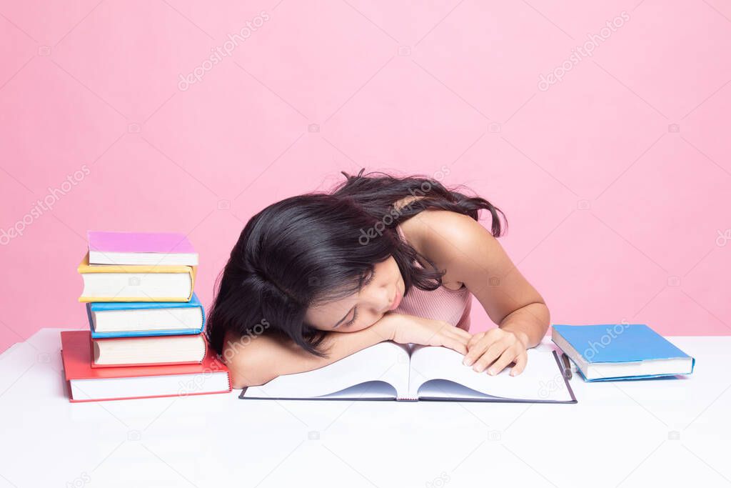 Exhausted Young Asian woman sleep with books on table on pink background
