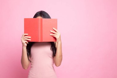 Genç Asyalı kadın, pembe arka planda yüzünü kaplayan bir kitap.
