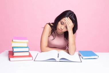 Bitkin düşmüş genç Asyalı kadın, pembe arka plan üzerine kitapları olan bir kitap okudu.