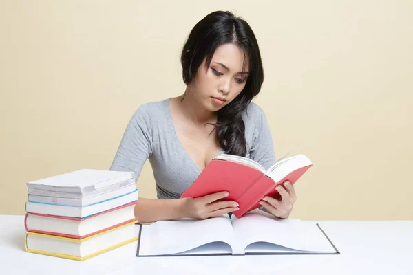 Young Asian woman read a book with books on table   on beige background