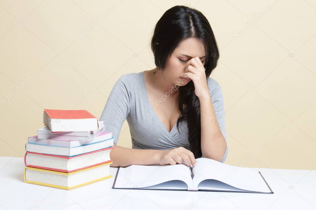 Exhausted Asian woman got headache read a book with books on table   on beige background