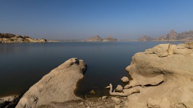 Jawai barajının berrak mavi gökyüzü ve Aravalli dağlarının seçici odak noktası Hindistan 'ın Rajasthan kentindeki Jawai' de sudaki yansıması.