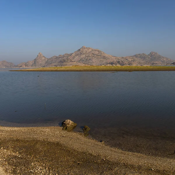 Jawai barajının berrak mavi gökyüzü ve Aravalli dağlarının seçici odak noktası Hindistan 'ın Rajasthan kentindeki Jawai' de sudaki yansıması.