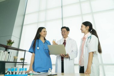 Asyalı doktorlar bir arada duruyor ve konuşmak için dizüstü bilgisayar kullanıyorlar..
