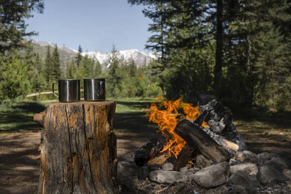 Two metal mugs near the fire on the background of the mountains
