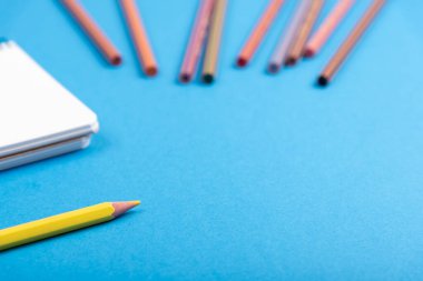 Sarı kalem, not defteri ve renkli kalemler kopya alanı ile mavi arkaplan üzerinde bulanıklaştı