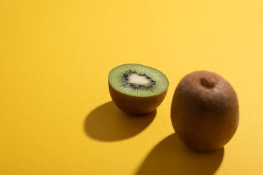 Yarım kivi odaklı ve bir bütün sarı karton üzerinde bulanık ve sert güneş ışığı ile aydınlatma