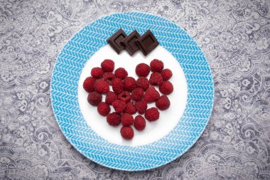 Ahududu ve çikolata karelerinin kalbi beyaz ve mavi tabağın üzerine yatıyordu. Romantik tatlı. Yüksek çözünürlük