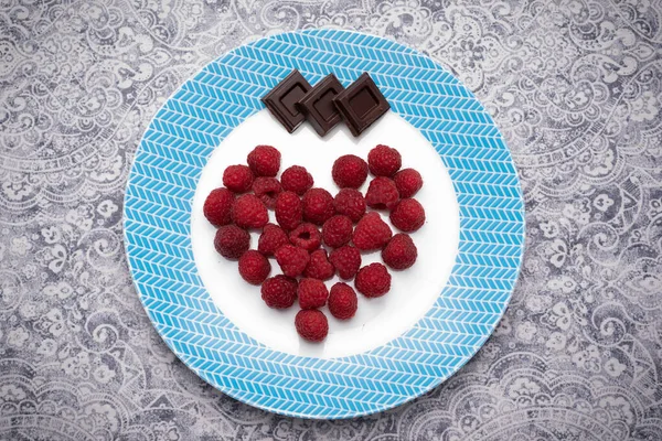 Ahududu ve çikolata karelerinin kalbi beyaz ve mavi tabağın üzerine yatıyordu. Romantik tatlı. Yüksek çözünürlük