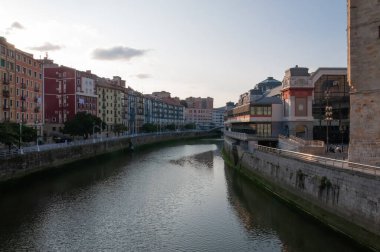Bilbao, Euskal Herria, İspanya - 09 04 2018: Ribera pazarında Nervion nehri ve gün batımında San Anton kilisesi. Açık mavi gökyüzü ve birkaç küçük bulut kopya alanı sunar