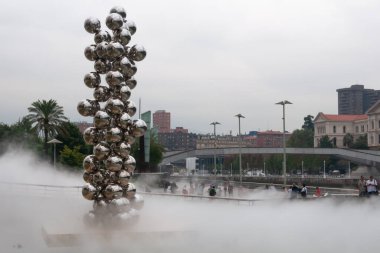 Bilbao, Euskal Herria, İspanya - 09 05 05 2018: Kapoor Büyük ağaç ve göz heykeli ve Fujiko Nakaya sis F.O.G. 08025 Guggenheim Müzesi 'nde. Yazın bulutlu bir gününde, bilinmeyen insanlar yürüyor.