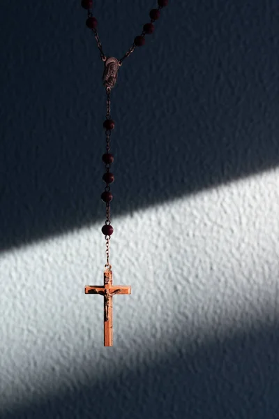 Rosary cross lit by sun hanging over a background diagonal light on coarse wrinkled aqua menthe wall. God enlightens people knowledge